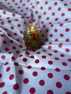 a jar filled with flowers sitting on top of a polka dot table cloth next to a lit candle