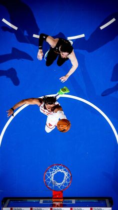 two women playing basketball on an indoor court with blue walls and white rims, overhead view from above