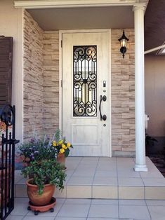 a white front door with two potted plants on the porch and an iron gate