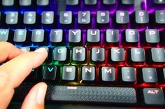 a person's hand is on the keys of a computer keyboard that has red, purple and blue lights