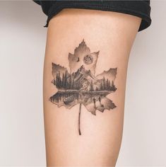 a woman's thigh with a leaf tattoo on the side of her leg that has a lake and trees in it