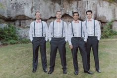 three men in suits and bow ties standing next to each other near a rock wall