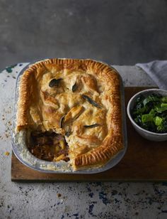 a pie sitting on top of a wooden cutting board next to a bowl of greens