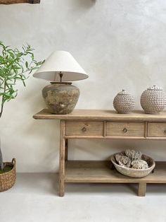 a wooden table with two vases and a lamp on it next to a potted plant