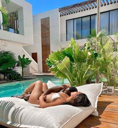 a woman laying on top of a white pillow next to a swimming pool with palm trees