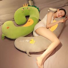 a young woman laying on top of a bed next to a pillow shaped like a caterpillar