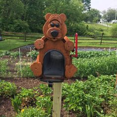 a wooden bear mailbox sitting in the middle of a garden