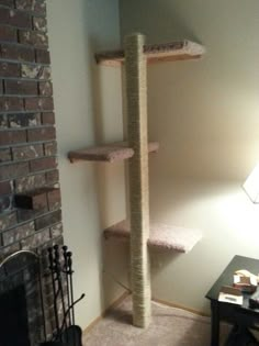 a cat tree in the corner of a living room next to a fire place and lamp