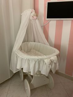 a white baby crib in a pink and white striped room with a tv on the wall