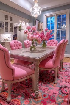 a dining room table with pink chairs and flowers in a vase on top of it