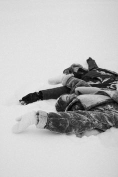 two people laying in the snow with their arms around each other and one person wearing a jacket