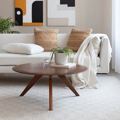 a living room with a white couch, coffee table and two paintings on the wall