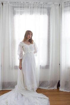 a woman standing in front of a window wearing a white dress with ruffled sleeves