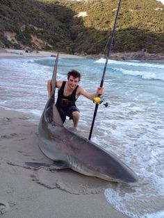 a man is holding onto a shark on the beach with a fishing rod in his hand