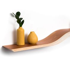 two yellow vases sitting on top of a wooden shelf next to a green plant