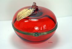 a red glass apple with a gold leaf on it's top sitting on a white surface