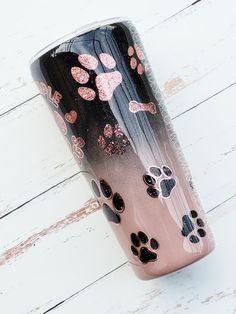 a pink and black tumbler with paw prints on the side sitting on a white wood floor