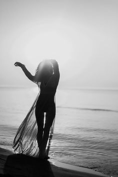 a woman standing on top of a beach next to the ocean holding her hand out