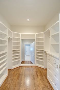 an empty walk in closet with white shelving and wood flooring on the side