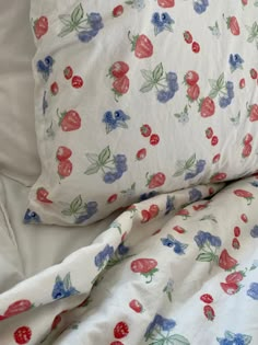 an unmade bed with white sheets and red, blue, and green flowers on it