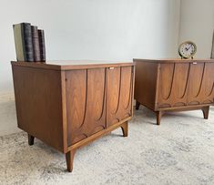 two wooden cabinets sitting on top of a carpeted floor next to a clock and books