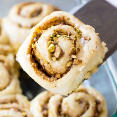 a close up of a cinnamon roll being held by a fork with other rolls in the background