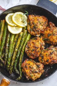 chicken and asparagus in a skillet with lemon wedges