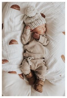 a baby laying on top of a bed wearing a knitted hat and striped outfit