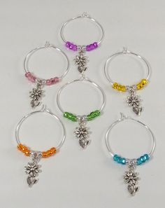 six pairs of hoop earrings with charms on each side and flowers in the middle, all different colors