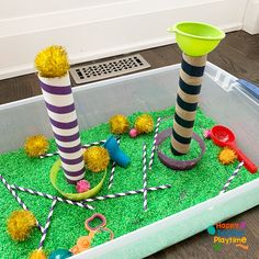 a plastic container filled with green grass covered in different types of toys and decorations on top of it