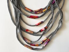 Embrace summer with a statement cord necklace that's anything but ordinary. This unique, multi-stranded textile yarn necklace is crafted from a delightful blend of soft, lightweight cotton and hand-painted beads. It's a layered masterpiece bursting with vibrant stripes and pops of color from red - purple - gold beads. It's the perfect summer accessory, adding instant sophistication to a simple t-shirt and jeans or elevating a flowy blouse.  This long fabric necklace combines a range of lengths from 7.8 to 15.7 inches, ensuring a comfortable fit that flatters any outfit. More than just a necklace, it's a piece of wearable art, a true conversation starter. Complete your bohemian or summer look, ditch the mass-produced jewelry and embrace the unique - this handcrafted scarf necklace  is a tru Multi-strand Black Necklace For Beach, Black Multi-strand Necklace For Beach, Tshirt Necklace, Yarn Necklace, Bohemian Scarves, Painted Beads, Hand Painted Beads, Black And White Scarf, Scarf Necklace