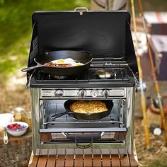 an outdoor stove with two pans on the burners and food cooking in it