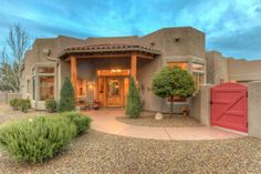 an adobe style home with red doors and green bushes in front of the entrance to it