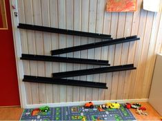 there are black shelves on the wall with toy cars in front of it and a door behind them