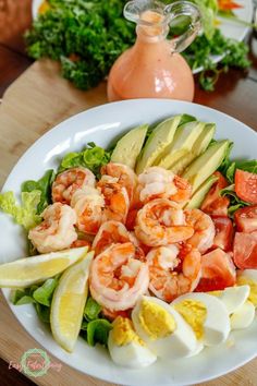 a salad with shrimp, avocado, tomatoes and lettuce on a white plate