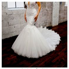 a woman in a white wedding dress standing on a wooden floor next to a brick wall