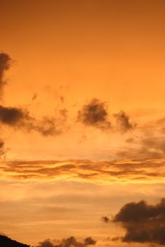 an airplane flying in the sky at sunset with clouds and mountains behind it as the sun sets