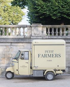 a small truck is parked in front of a stone wall and fence with trees behind it