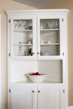 a white china cabinet with glass doors and two bowls on it's top shelf