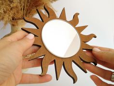 two hands are holding a mirror that is shaped like a sun