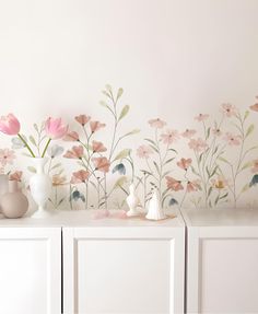 a white dresser topped with vases and flowers on top of it next to a wall