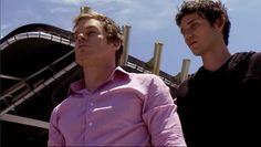 two men standing next to each other in front of a roller coaster at an amusement park