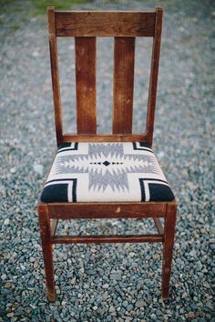 a wooden chair with a black and white seat cushion on top of gravel covered ground