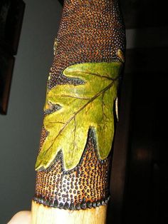 a close up of a person holding a wooden object with leaves and dots on it