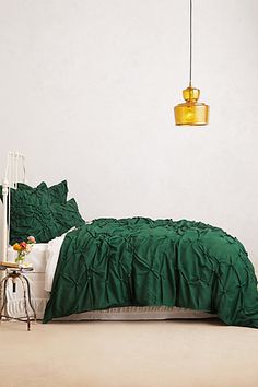 a bed with green comforter and pillows in a white room next to a lamp