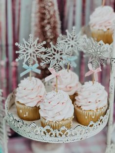 cupcakes with pink frosting and snowflakes are on a cake stand