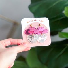 a person holding up a pair of pink and white earrings with hearts on them,