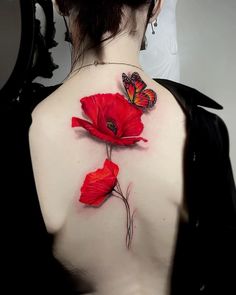 a woman's back with two red flowers on her shoulder and a butterfly flying over it