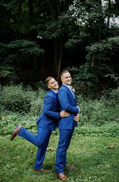 two men in blue suits are hugging each other on the green grass with trees in the background