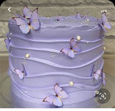 there is a purple cake with butterflies on the frosting and icing, along with pearls